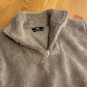 Beige tjock-tröja med halv dragkedja från BikBok - Mysig beige lurvig tröja från BikBok i storlek M. Tröjan har en halv dragkedja framtill, perfekt för kyliga dagar. Tillverkad i återvunnet material och har lång ärm för extra värme.