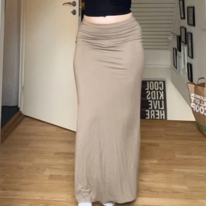 Beige långkjol från Nelly - Säljer en beige maxikjol från Nelly med låg midja och figurnära passform. Kjolen är enkel och stilren utan mönster eller extra detaljer, perfekt att matcha med olika toppar. Materialet känns mjukt och stretchigt. Storlek S. Aldrig använd