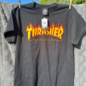 Svart helt ny Thrasher t-shirt M - Svart t-shirt från Thrasher med ikoniskt flames-tryck i rött och gult på bröstet. Klassisk passform och rund halsringning, perfekt för en streetwear-look. Helt ny med kapparna kvar. Nypris 550kr. Strl M