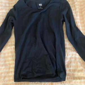 Svart långärmad topp från 157 - En enkel svart långärmad topp från 157 i mjuk bomullsblandning med lite stretch. Perfekt basplagg med rund halsringning och smal passform. Passar till allt och är superbekväm att ha på sig.