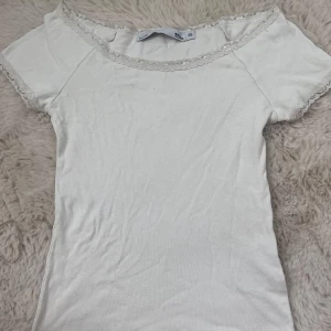 Vit topp med spets - Söt vit topp från 157 i storlek XS. T-shirten har korta ärmar och är dekorerad med spetsdetaljer längs halsringningen och ärmsluten. Perfekt för dig som gillar en enkel men ändå gullig stil.