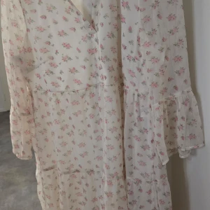 Blommig kortklänning från Vero Moda - Söt kortklänning från Vero Moda i vitt med små rosa blommor. Klänningen har omlott-skärning, trekvartsärm med volang och lätt, luftig känsla. Perfekt för vår och sommar! Ny med lapp.