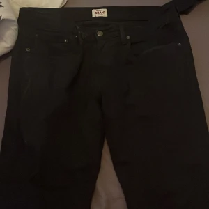 Svarta jeansbyxor från Grant - Svarta jeansbyxor från Grant med klassisk femficksdesign och raka ben. Byxorna har knapp och dragkedja framtill samt bälteshällor i midjan. Perfekta för en stilren och enkel look.