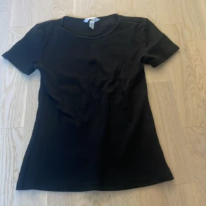 Svart ribbad t-shirt - En enkel svart ribbad t-shirt med rund halsringning och korta ärmar. Perfekt basplagg som passar till det mesta och är lätt att matcha med andra plagg.