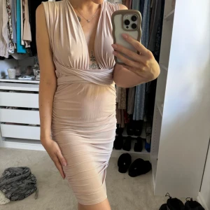 Ljusrosa/nude omlottklänning med öppen rygg - Säljer en ljusrosa/nude tight omlottklänning med djup v-ringning och öppen rygg. Klänningen har draperade detaljer och är ärmlös med långa band som man kan knyta hur man vill. Perfekt för dig som vill ha en elegant och figurnära look. Klänningen är använd 2 gånger! 