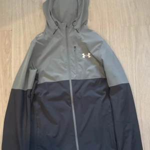 Grå vindjacka från Under Armour - Säljer min under Armour jacka för använder inte den är i bra skick och riktig snygg skriv om intresse priset kan diskuteras. Jackans storlek är i S men passar M(påse ingår)