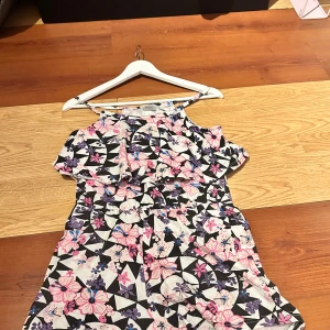 Blommig oneshoulder klänning från bpc - Säljer en färgglad oneshoulder klänning från bpc med blommigt mönster i rosa, lila och svart. Klänningen har volang upptill och resår i midjan för en bekväm passform. Perfekt för varma dagar!