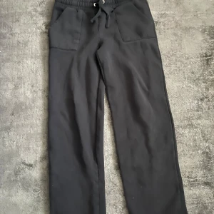 Svarta mjukisbyxor med dragsko - Svarta mjukisbyxor med bred resår i midjan och dragsko. Byxorna har raka ben och två stora fickor framtill. Perfekta för en avslappnad stil.