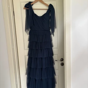 Marinblå långklänning med volanger från Lace & Beads - Säljer en superfin marinblå långklänning från Lace & Beads med flera lager volanger och justerbara rosetter på axlarna i modellen Ophelia Maxi från asos! Aldrig använd och har därför prislappen kvar! Nypris 1489 kr