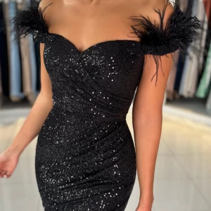 Svart glittrig långklänning med fjädrar - Supersnygg svart långklänning med glittriga paljetter, offshoulder design och sits! Köpte den i år (1maj) inför balen.Köpte den för 3000 och säljer för 1700!! Säljer pga att den inte kommer till nån användning 💕!