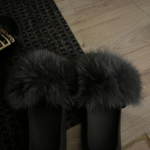 Svarta tofflor med grå päls - Säljer ett par svarta tofflor med fluffig grå päls upptill. Perfekta att glida runt i hemma för en mysig känsla. Snygg och trendig design som sticker ut.