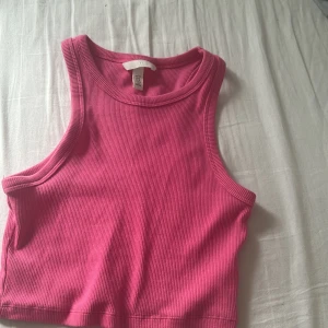 Rosa ribbad croppad linnetopp från  H&M - Säljer en rosa ribbad croppad linnetopp från H&M. Toppen har breda axelband och rund halsringning, perfekt för varma dagar eller som ett lager under en skjorta.