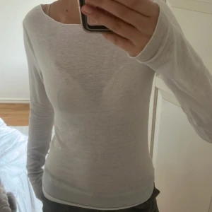 Vit långärmad topp - Säljer en enkel och stilren vit långärmad topp i tunnare material. Perfekt att ha som basplagg eller under en kofta. Sitter tight och har rund halsringning.