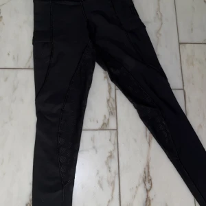 Svarta ridleggings från Maya Delorez - Svarta ridleggings från Maya Delorez i storlek 3XS. Byxorna har diskreta logodetaljer och är tillverkade i ett stretchigt syntetmaterial som ger bra rörelsefrihet. Perfekta för ridning med förstärkta partier på insidan av benen.