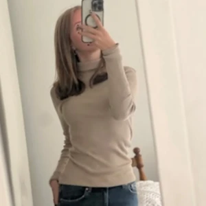 Beige polotröja - Säljer en stilren beige polotröja med lång ärm. Tröjan är figurnära och passar perfekt till jeans eller kjol. Enkel och tidlös design som funkar året runt.