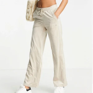 adidas Originals beige velour vida mjukisbyxor EU 34 - Säljer ett par adidas beige mjukisbyxor med breda ben och resår i midjan. Byxorna har snörning i midjan och är gjorda i ett mjukt, sammetsliknande material. Gulddetaljer. Perfekta för en avslappnad men snygg stil. Har ett litet märke som inte går bort i tvätten, syns på bilderna!