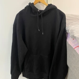 Svart hoodie med huva och ficka - En klassisk oversized svart hoodie med huva och en stor magficka. Perfekt för en avslappnad stil och enkel att matcha med det mesta. Mjuk och bekväm, passar både till vardags och när du vill mysa hemma.