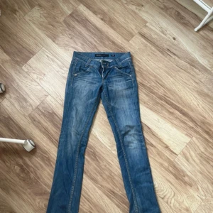 Lågmidjade jeans - Säljer ett par klassiska blå jeansbyxor från Miss Sixty med normal passform och låg midja. Byxorna har raka ben, fem fickor och stängs med dragkedja och knapp. Perfekta för en avslappnad stil. Dock är knappen lite lös men jag Har inga problem med att knäppa dom