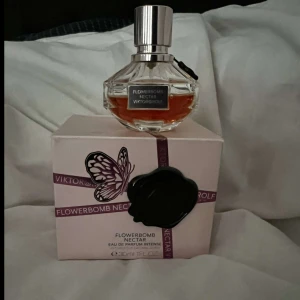 Flowerbomb Nectar Eau de Parfum från Viktor & Rolf - En exklusiv parfym i glasflaska med silverfärgad kork. Doften Flowerbomb Nectar kommer i en elegant förpackning med fjärilsmotiv och svart sigill. Flaskan rymmer 30 ml och har en rosa-orange vätska.