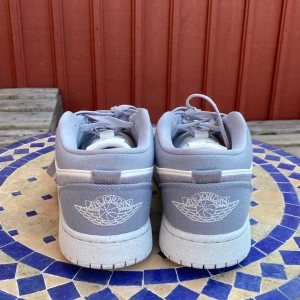 Nike Air Jordan 1 Low i grått och vitt - Säljer ett par Nike Air Jordan 1 Low i stilren grå och vit färg. Skorna har klassisk snörning, perforerad tå och ikonisk Air Jordan-logga broderad på hälen. Perfekta sneakers för dig som gillar streetwear och sportig stil.