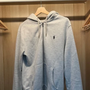 Ljusgrå hoodie från Ralph Lauren - Säljer en stilren ljusgrå hoodie från Ralph Lauren med dragkedja och huva. Anledningen till varför jag väljer att sälja denna är pga att jag växt ur den. Fick den i julklapp men är i stort sätt som ny👍