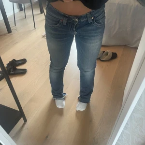 Blå jeansbyxor från True Religion - Säljer ett par klassiska blå jeansbyxor från True Religion med ikonisk patch bak i midjan. Byxorna har normal passform, låg midja och raka ben/bootcut. Perfekta för dig som gillar en tidlös jeansstil.