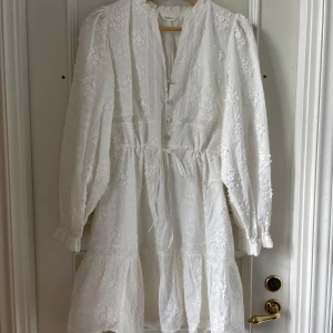 Vit blommig klänning från Dobber - Superfin vit klänning från Dobber med broderade blommor, knappar framtill och knyt i midjan. Klänningen har långa ärmar med lätt puff och volang nertill. Perfekt för sommarens tillfällen eller studenten!! Använd en gång på min studentmottagning förra året 💕💕