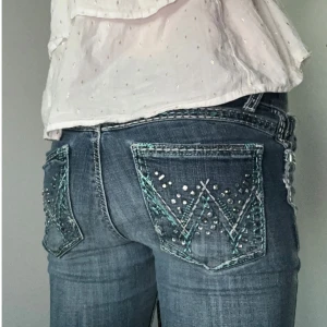 jeans - Säljer ett par blå jeans med slitningar på låret och knät. Bakfickorna har detaljerade broderier i turkos och silverfärgade nitar. 💝💝Jeansen är lite slitna på ryggen, som visas på bilden.🙏