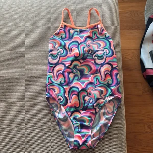 Färgglad baddräkt från Funkita - Säljer en färgglad baddräkt från Funkita med  mönster i rosa, lila, grön, orange och blå. Baddräkten har smala axelband, öppen rygg (dimond back) och är tillverkad i polyester. Perfekt för simträning eller bad. Använd fåtal gånger. Storlek ,14 år, 164.