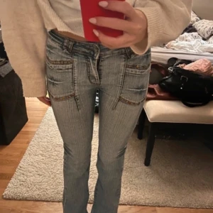 Ljusblå bootcut jeans med nitar - Säljer ett par ljusblå jeans med bootcut passform och dekorativa nitar på fickorna. Jeansen har låg midja och markerade sömmar framtill och baktill. Perfekta för dig som gillar en retroinspirerad stil.