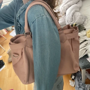 Ljusrosa handväska med axelrem - Säljer en ljusrosa handväska med både handtag och avtagbar axelrem. Väskan har silverfärgade metalldetaljer och ett Birkin liknande spänne framtill. Rymlig insida och ett litet fack på insidan. Har en liten fläck som var där när jag köpte den men inget som man tänker på. Längd:29cm bred: 42cm. Här av dig om du har några frågor eller funderingar 💕