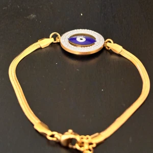 Guldarmband med blått öga och stenar  - Snyggt guldarmband med ett blått öga i mitten, omringat av glittrande stenar. Armbandet har en tunn kedja och ett klassiskt lås. Köpt i italien.