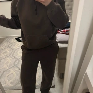 Mörkbrun hoodie med ficka - Säljer en mörkbrun hoodie med huva och dragsko. Tröjan har en stor magficka och ribbade muddar vid ärmslut och nederkant. Perfekt för en avslappnad stil.