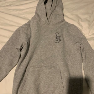 Grå hoodie från Brand Store Kids - Säljer en ljusgrå hoodie från Brand Store Kids med en söt björn med ballong tryckt på bröstet. Tröjan har huva och långa ärmar, perfekt för en avslappnad stil. Mjuk och skön bomullsblandning.