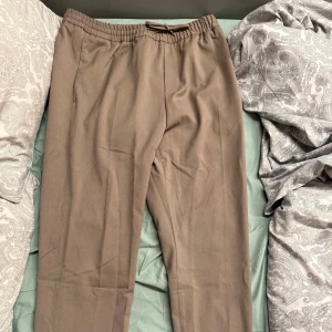 Bruna ”kostymbyxor” med resår i midjan - Säljer ett par bruna kostymbyxor med rak passform och resår i midjan. Byxorna har en klassisk look och är perfekta för en stilren outfit. Inga synliga fickor eller detaljer framtill. Finns i Stockholm annars kan fraktas. 