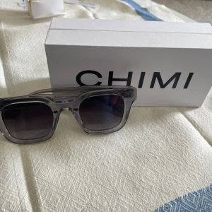Gråa solglasögon från CHIMI - Snygga solglasögon från CHIMI i transparent grå färg med rektangulära bågar. Modellen är 04 GREY och har mörka glas. Perfekt accessoar för att lyfta din stil.