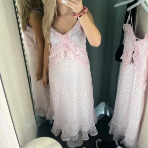 Ljusrosa blommig långklänning med volang och knyt - Superfin ljusrosa långklänning med små blommor, volangdetaljer och knyt framtill. Klänningen har ärmlös design och volangkant nertill. Perfekt för sommarens tillfällen! Enbart använd en gång!💕