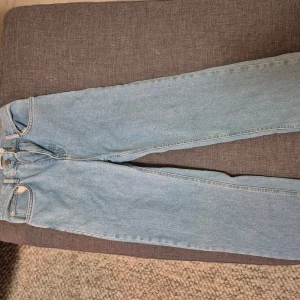 Ljusblå jeans från NA-KD med råa kanter - Säljer ett par ljusblå jeans från NA-KD med raka ben och råa, fransiga benslut. Jeansen har hög midja och klassisk femficksdesign. Perfekta för en avslappnad och trendig look.