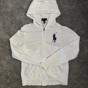 Sällsynt Ralph Lauren zip-hoddie - Säljer en vit hoodie från Polo Ralph Lauren med dragkedja och huva. Tröjan har det klassiska mörkblå broderade polospelar-loggan på bröstet och två fickor framtill. Perfekt för en avslappnad stil. Har en liten fläck på slutet av armen som du kan se på bilden men går säkert att få bort