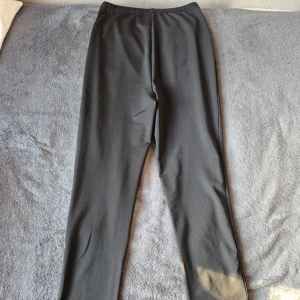 Svarta byxor med slits från SHEIN - Svarta byxor från SHEIN i storlek XS. Endast använda en gång. Byxorna har en rak passform och är tillverkade i ett stretchigt syntetmaterial. Nedtill på benen finns en slits som ger en snygg detalj. Perfekta att styla med sneakers eller boots.