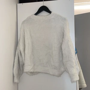 Vit fluffig stickad tröja från H&M - Mysig vit stickad tröja från H&M med fluffig textur. Tröjan har lång ärm och rund halsringning, perfekt för kyligare dagar. Enkel och stilren design som passar till många outfits.
