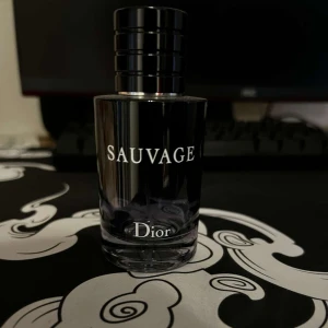 Sauvage parfym från Dior - Säljer en Sauvage parfym från Dior. Flaskan är genomskinlig med svart lock och tydlig vit text. Doften är känd för sin fräscha och maskulina karaktär, perfekt för dig som vill sticka ut.