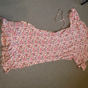 Blommig omlottklänning Saint Tropez i XS  - Använd fåtal gånger. Supersöt klänning med blommigt mönster i rosa, vit, blå och gul. Omlottmodell med knyt i midjan, v-ringning och volangkant nertill. Halvlånga ärmar och mjukt, lätt material – perfekt för varma dagar.