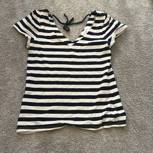 Randig v-ringad topp med knyt - Snygg randig topp med svart och vit design, v-ringning och knyt i nacken. Kortärmad och i mjukt bomullsmaterial, perfekt för en avslappnad och trendig look.