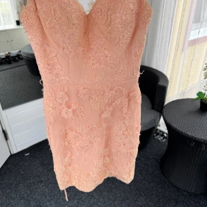 Ljusrosa spetsklänning med pärlor - Superfin ljusrosa/aprikos färgad kortklänning med blommig spets, pärldetaljer och smala axelband. Klänningen har v-ringning, figurnära passform och knappar i ryggen. Pris går att diskuteras!