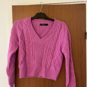 Rosa stickad v-ringad tröja - Säljer en rosa stickad tröja från new yorker med snyggt kabelstickat mönster och v-ringning. Tröjan har långa ärmar och ribbade muddar vid ärmslut och nederkant. Aldrig använd endast testad