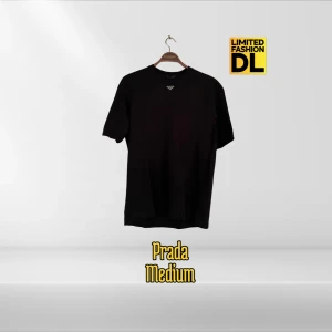 Svart t-shirt från Prada - Stilren t-shirt från Prada i svart. Klassisk passform, rund halsringning och korta ärmar. Diskret Prada-logo framtill. Perfekt för dig som gillar minimalistisk och exklusiv design. Ikonisk Prada-design som fungerar både till vardag och mer stilrena sammanhang 	•	Lätt att matcha med jeans, kostymbyxor eller shorts 	•	Perfekt plagg för dig som uppskattar kvalitet, komfort och varumärkesstatus