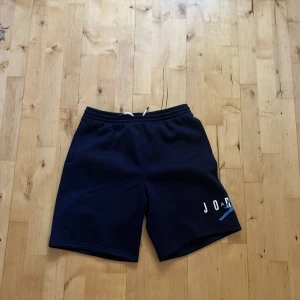 Mörkblå Jordan shorts XL - Snygga mörkblå shorts från Jordan med vit och blå logga på benet. De har elastisk midja med snörning och är tillverkade i mjukt material, perfekta för sport eller chill. Klassisk och sportig look med normal passform. Passar folk från 163-175 cm.