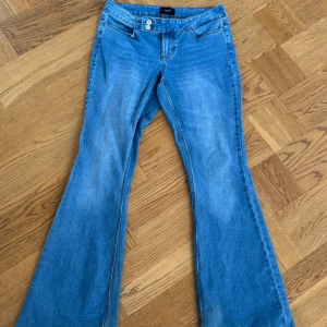 Blå bootcut jeans från Vero Moda - Snygga blå bootcut jeans från Vero Moda med klassisk femficksdesign och dubbla knappar i midjan. Jeansen har låg midja och är tillverkade i mjukt denimtyg. Perfekta för dig som gillar retrovibbar och vill ha ett par jeans med utsvängda ben.