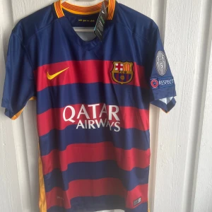 FC Barcelona Messi 10 matchtröja Nike - Barça matchtröja med Messi 10 på ryggen, tillverkad av Nike. Tröjan har breda blå och röda ränder, gula detaljer och klubbmärke på bröstet. Qatar Airways-logga framtill och Champions League-märke på ärmen. Materialet är lätt och andas, perfekt för fotboll.